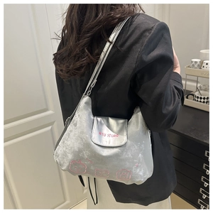 Details der silbernen Metallic-Umhängetasche mit rosa AITU STUDIO Aufdruck und Stickerei