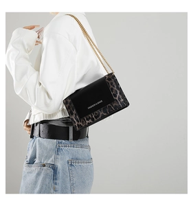 Detail of trendy leopard print chain bag featuring a black leather flap and gold strap