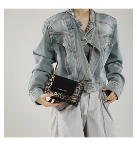 Detail of a leopard print crossbody bag with gold chain and black flap on a denim jacket