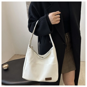 Détail du sac hobo en cuir PU blanc avec poche avant et étiquette décorative marron