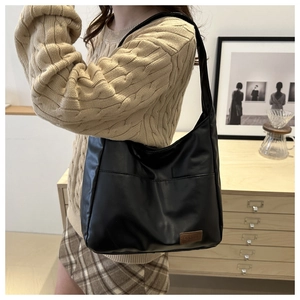 Détail du sac hobo en cuir PU noir avec étiquette de mode sur pull en maille beige