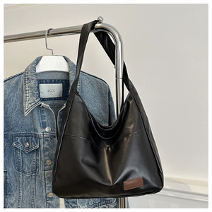 Détail d'un grand sac hobo noir en similicuir avec étiquette de mode sur veste en jean