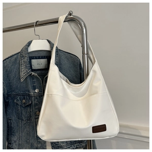 Détail du grand sac cabas en cuir PU blanc avec étiquette mode et poche avant sur denim