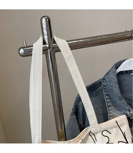 Dettaglio borsa tote in tela bianca con linee artistiche nere su gruccia metallica