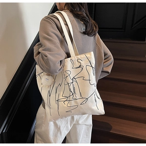 Vista posteriore dettagliata della borsa tote in tela beige con arte astratta e ciondolo