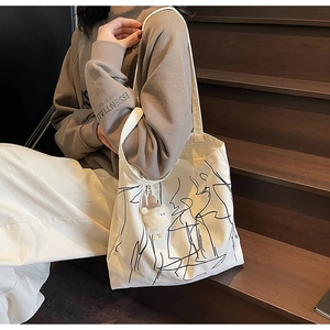 Dettaglio di una borsa tote in tela beige con arte astratta e ciondolo di peluche