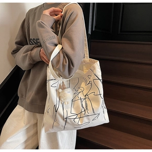 Dettaglio della borsa tote in tela bianca con arte astratta nera e ciondolo a pompon