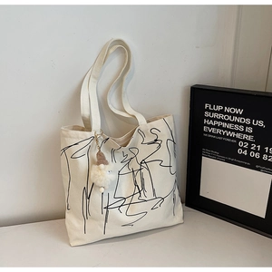 Dettaglio borsa tote in tela bianca con grafica astratta nera e ciondolo di peluche