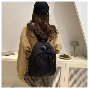 Rear view of a minimalist black nylon backpack on a model in a natural lifestyle setting