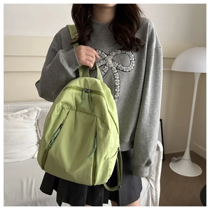 Detailed close-up of light green nylon backpack held by model in minimalist room