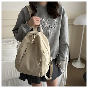 Minimalist beige nylon backpack shown on model in a cozy indoor lifestyle setting