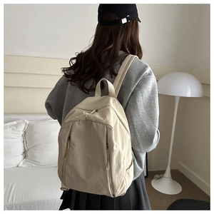 Beige nylon backpack with large main compartment shown in a cozy bedroom setting