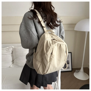 Detail view of a beige nylon backpack featuring multiple zipped compartments and minimalist design