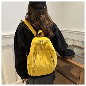 Rear view of model wearing a ginger yellow nylon backpack with dual vertical zipper pockets