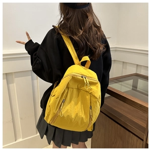 Lightweight mustard yellow nylon backpack worn by a model in a minimalist indoor setting