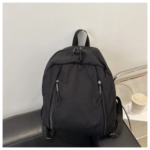Detail of a lightweight black backpack with dual vertical zipper pockets on a leather bench