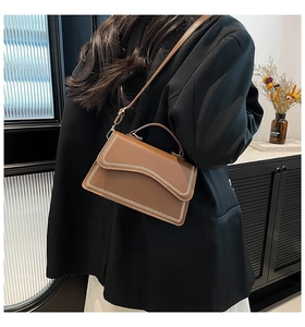 Brown leather crossbody bag detail with wave-shaped flap and cream V-stitch edging