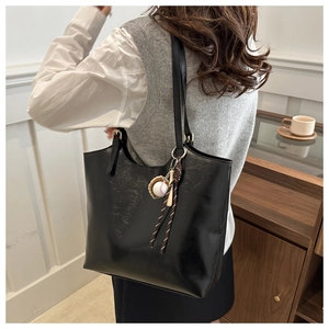 Detail of glossy black tote bag with unique baseball keychain accessory and slim strap