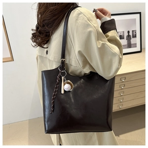 Deep brown oversized soft leather tote bag with baseball charms shown on shoulder