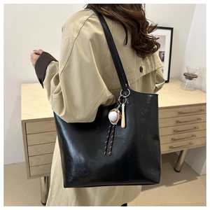 Close-up of black glossy leather tote bag with baseball charm on a trench coat