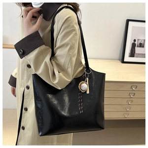 Large black leather tote bag with baseball pendant worn on shoulder over khaki coat