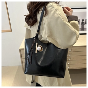 Detail view of a black soft leather tote bag featuring a creative baseball theme charm