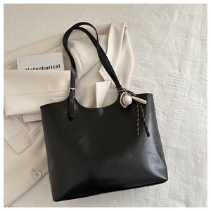 Detail of minimalist black leather tote bag with creative baseball pendant on blazer