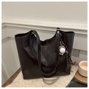 Close-up of vintage dark brown faux leather tote bag with baseball charm on wooden desk
