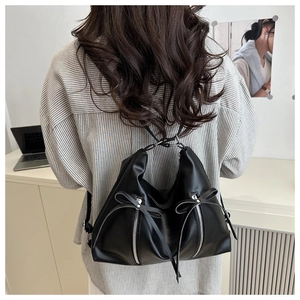Detail of black faux leather tote bag with silver zippers and decorative bows on straps