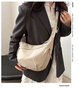 Detail of beige crescent crossbody bag with nylon texture and adjustable strap on a model