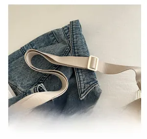 Detail of adjustable beige woven shoulder strap on blue denim crossbody bag