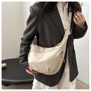 Detail showing the cream nylon fabric texture and zipper pocket of the crescent bag