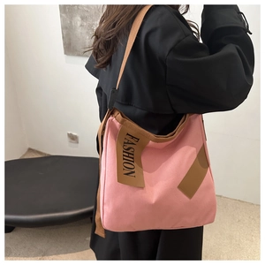 Vue latérale du grand sac cabas en toile rose avec des lanières marron sur un manteau noir