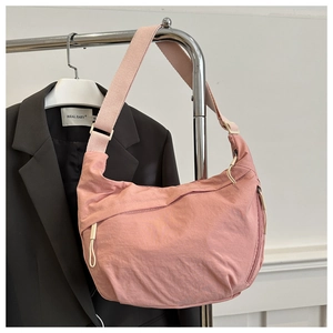 Close-up of pink nylon crescent bag with zipper details and wide crossbody strap
