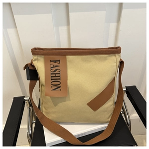 Détail d'un cabas en toile beige avec étiquettes en cuir marron et large bandoulière
