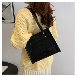 Detail of black faux leather tote bag with crocodile pattern and metal rivet accents