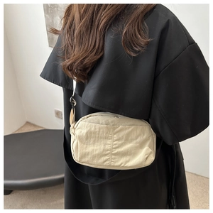 Detail of a beige nylon crossbody bag with crinkled texture on a model wearing black coat