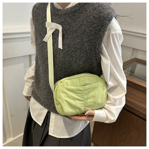 Detail of light green nylon crossbody bag with white bow accent on the strap