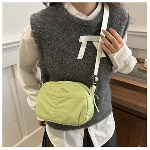 Detail of light green nylon crossbody bag with adjustable strap worn by a model