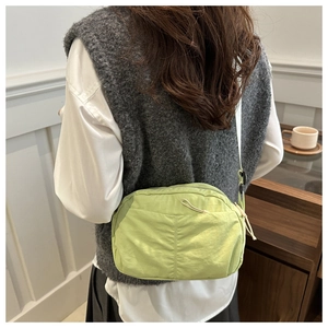 Close-up of pistachio green nylon crossbody bag with drawstring pocket and white strap