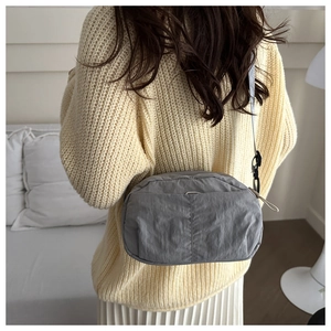Gray nylon crossbody bag showing the front compartment and textured finish on model