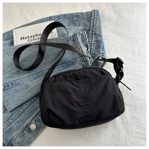 Detail of minimalist black nylon crossbody bag with adjustable strap and decorative stitching
