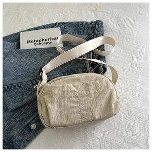 Detail of a beige nylon crossbody bag featuring natural crinkle texture and wide strap