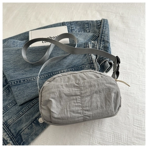 Detail shot of a grey nylon crossbody bag with adjustable strap and textured fabric