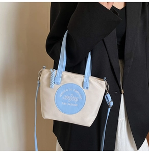 Détail d'un mini sac cabas bicolore en nylon avec broderie enjoy porté par un mannequin