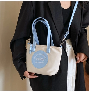 Gros plan sur un sac cabas blanc crème avec anses bleu clair porté par un mannequin