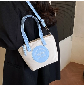 Détail du sac bandoulière en nylon bicolore porté par un mannequin avec sangle bleue