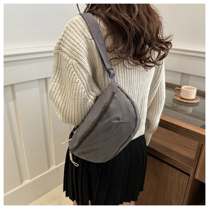 Close-up of a charcoal grey nylon crossbody bag shown on a model in a knit sweater