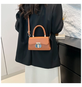 Brown leather crossbody bag with gold twist lock shown styled on a model in a black blazer