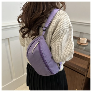 Detail of adjustable strap and buckle on a purple nylon crossbody bag worn by model
